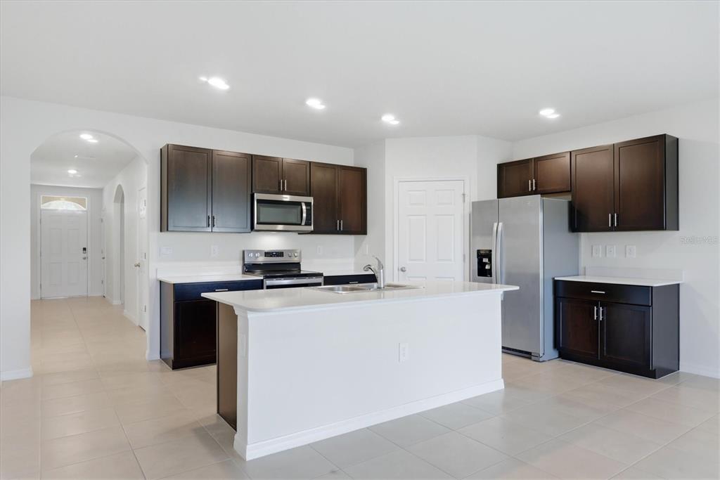A kitchen features dark wood cabinets, white countertops, stainless steel appliances, and a central island — 25118 DOREDO DRIVE, PUNTA GORDA, FL