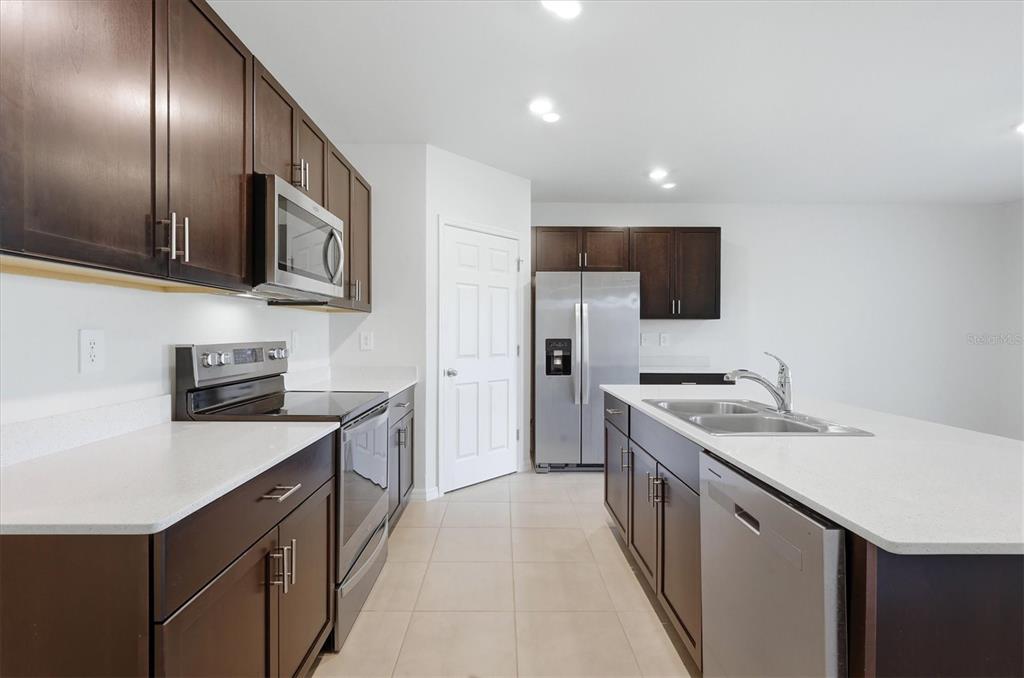 A kitchen features dark wood cabinets, stainless steel appliances, and a white quartz island countertop — 25118 DOREDO DRIVE, PUNTA GORDA, FL