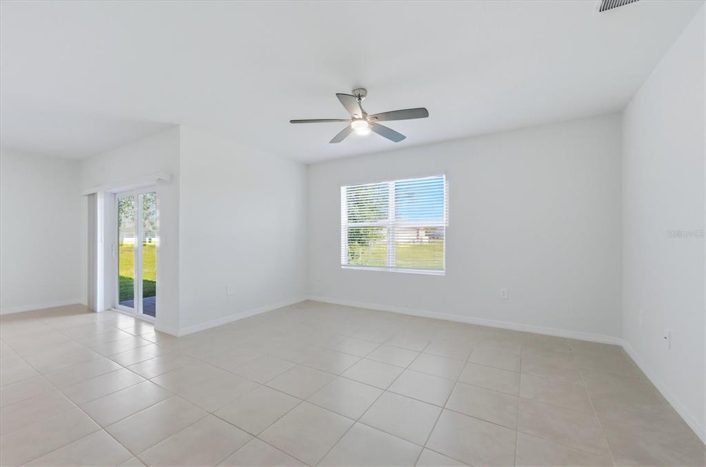 A bright, empty room features white walls, light tile flooring, a ceiling fan, and sliding doors — 25118 DOREDO DRIVE, PUNTA GORDA, FL
