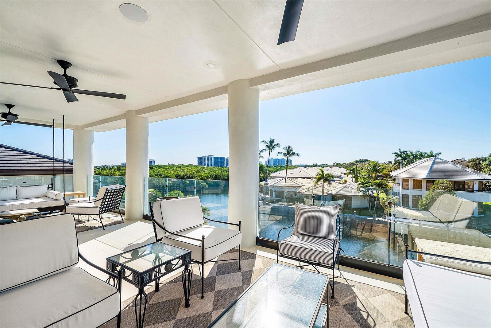A covered outdoor balcony features patio furniture, glass railings, and views of a canal — 5344 Boca Marina Circle N, Boca Raton FL 33487, BOCA RATON, FL