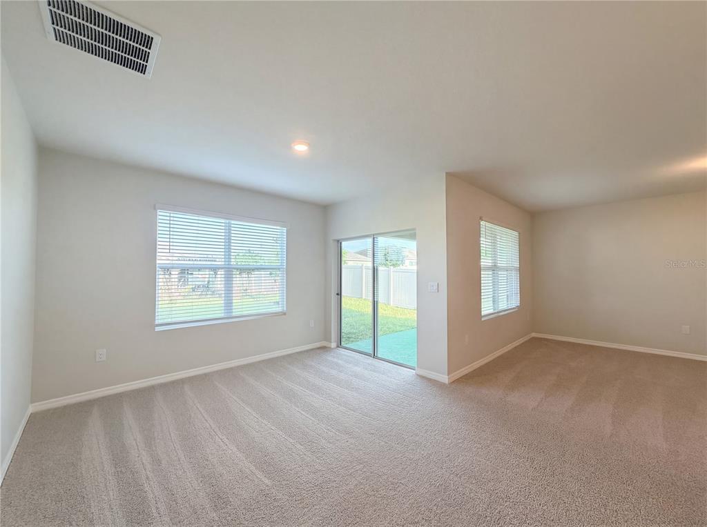 An empty living room features beige carpet, neutral walls, a sliding glass door, and windows — 1818 IRBY COURT, TAVARES, FL