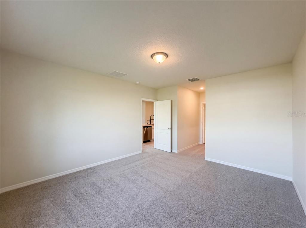 An empty room with beige walls, gray carpet, a ceiling light, and two open doorways — 1818 IRBY COURT, TAVARES, FL
