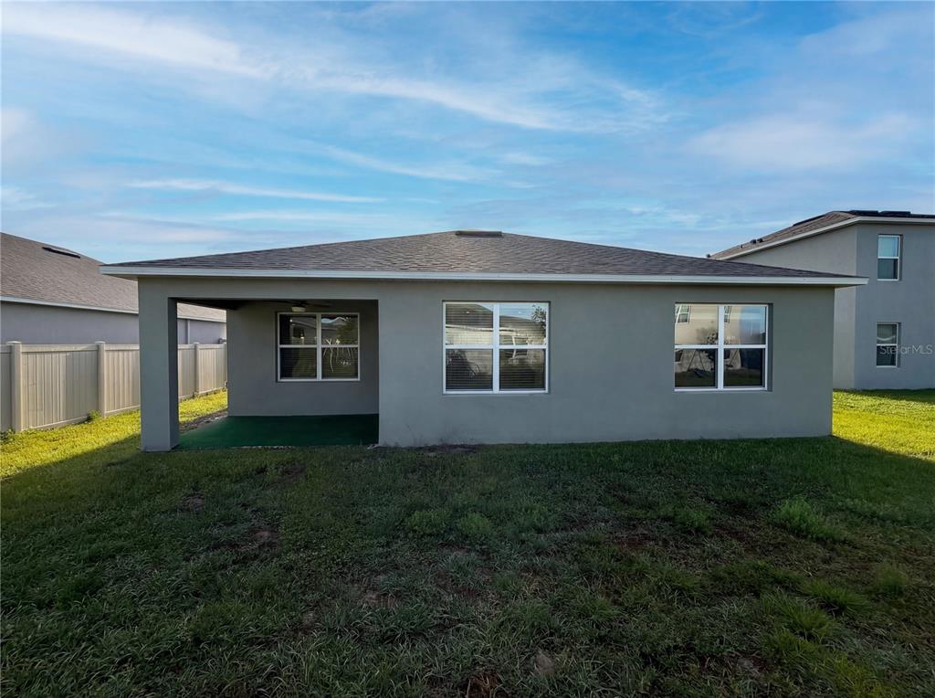 The rear exterior of a single-story house features a covered patio and a grassy yard — 1818 IRBY COURT, TAVARES, FL