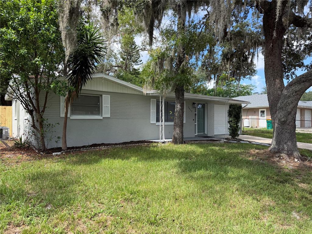 A single-story gray house with a white garage door and large oak trees in front — 5632 FRONT DRIVE, HOLIDAY, FL