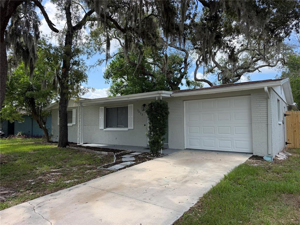A single-story house with a light gray brick exterior, a white garage door, and trees — 5632 FRONT DRIVE, HOLIDAY, FL