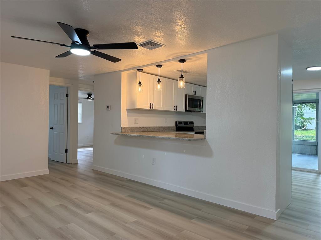 A kitchen with white cabinets and granite countertops overlooks a living area with wood flooring — 5632 FRONT DRIVE, HOLIDAY, FL