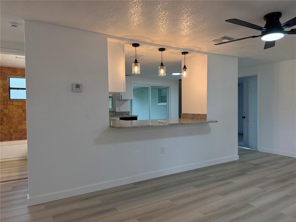 A kitchen pass-through with granite countertops and pendant lights overlooks a living area — 5632 FRONT DRIVE, HOLIDAY, FL