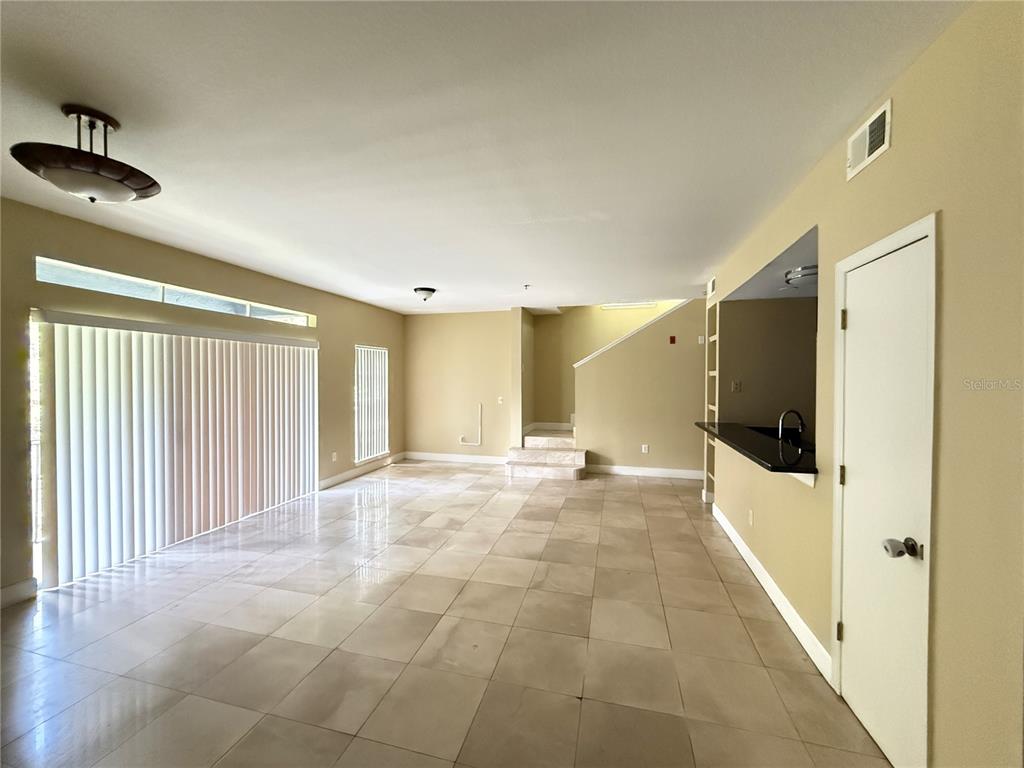 An open-concept living area features light-colored tile flooring, beige walls, and a staircase — 13212 ARBOR ISLE DRIVE UNIT 201, TAMPA, FL