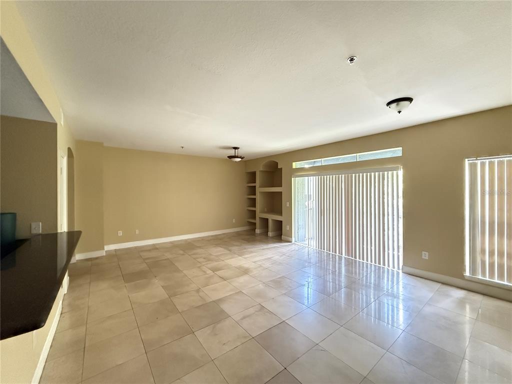 An open living area features beige walls, tiled floors, built-in shelving, and sliding glass doors — 13212 ARBOR ISLE DRIVE UNIT 201, TAMPA, FL