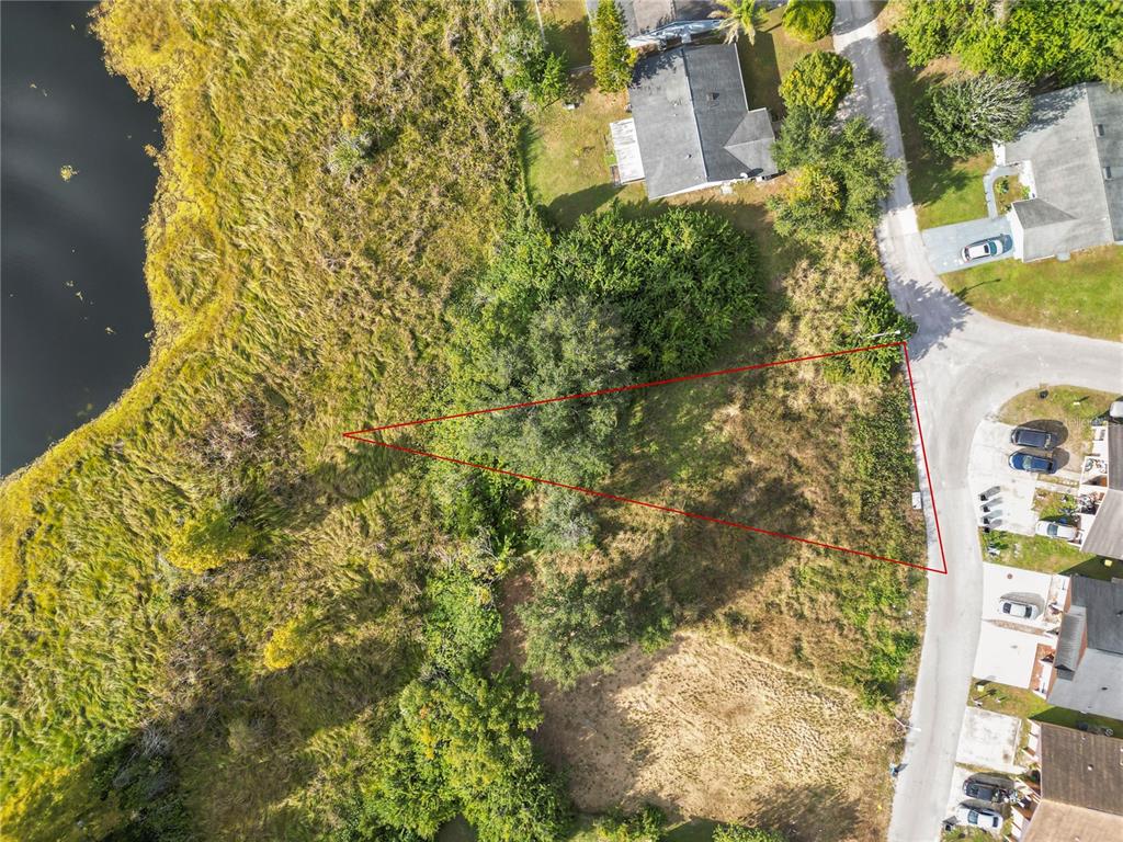 An aerial view shows a vacant, triangular-shaped lot situated between a road and a lake — CAPTIVA POINT, LAKELAND, FL
