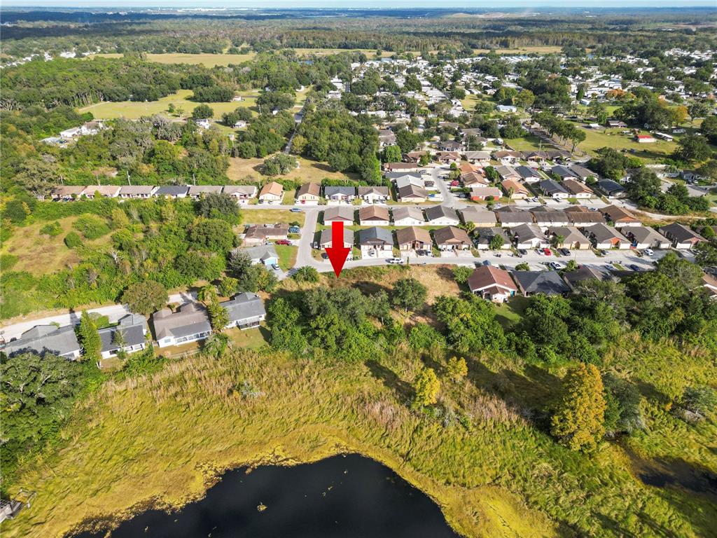An aerial view shows a vacant, tree-covered lot marked by a red arrow near a pond — CAPTIVA POINT, LAKELAND, FL