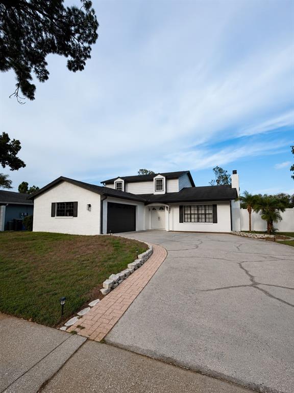 A white two-story house with a black roof and a cracked concrete driveway — 16209 W COURSE DRIVE, TAMPA, FL