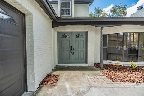 A white brick house exterior features a gray double front door and a garage — 16209 W COURSE DRIVE, TAMPA, FL