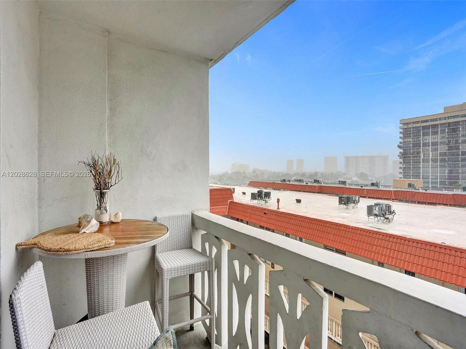 A balcony features a small round table, two wicker chairs, and a view of rooftops — 3113 S Ocean Dr # 603, Hallandale Beach FL 33009, HALLANDALE BEACH, FL