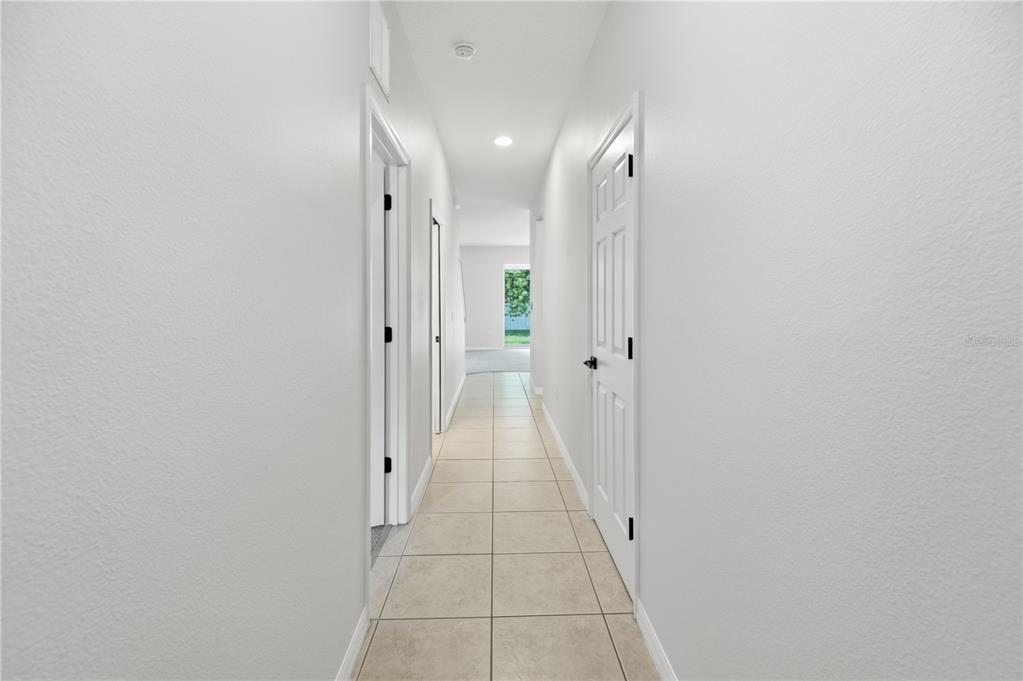 A long hallway with light-colored tile flooring and white walls leads to an exterior doorway — 3420 HOME TOWN LANE, ST CLOUD, FL