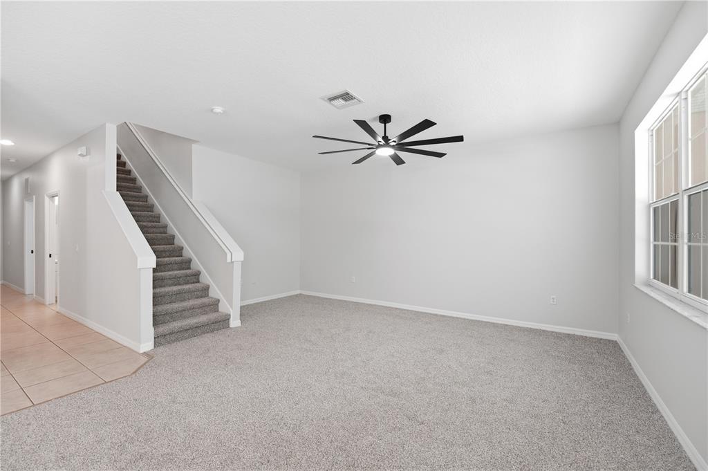 A carpeted living room features a staircase with a white railing and a ceiling fan — 3420 HOME TOWN LANE, ST CLOUD, FL