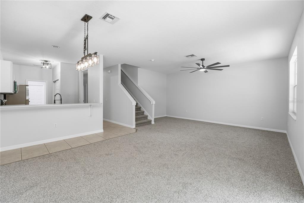A living room with gray carpet, a ceiling fan, and stairs leading to an upper level — 3420 HOME TOWN LANE, ST CLOUD, FL