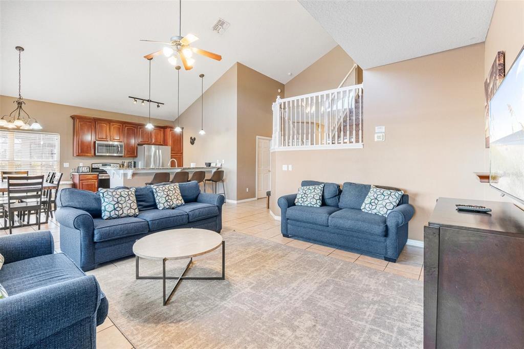 A living room with blue sofas, a round coffee table, and an open kitchen — 8019 ACADIA ESTATES COURT, KISSIMMEE, FL