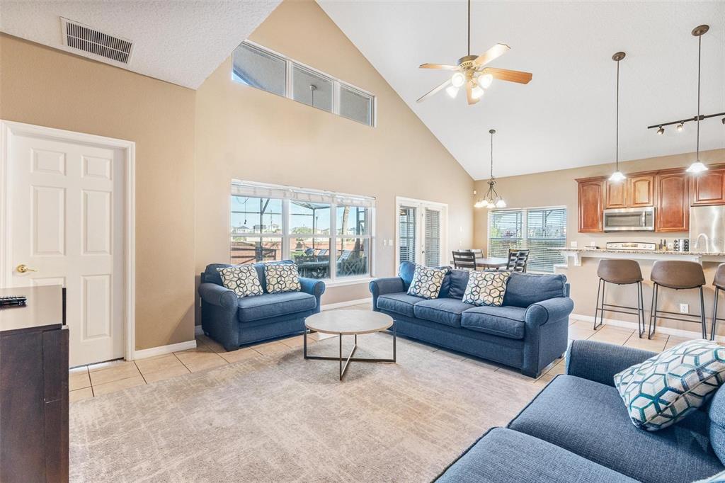 A living room with vaulted ceilings, blue sofas, and an open kitchen with bar seating — 8019 ACADIA ESTATES COURT, KISSIMMEE, FL