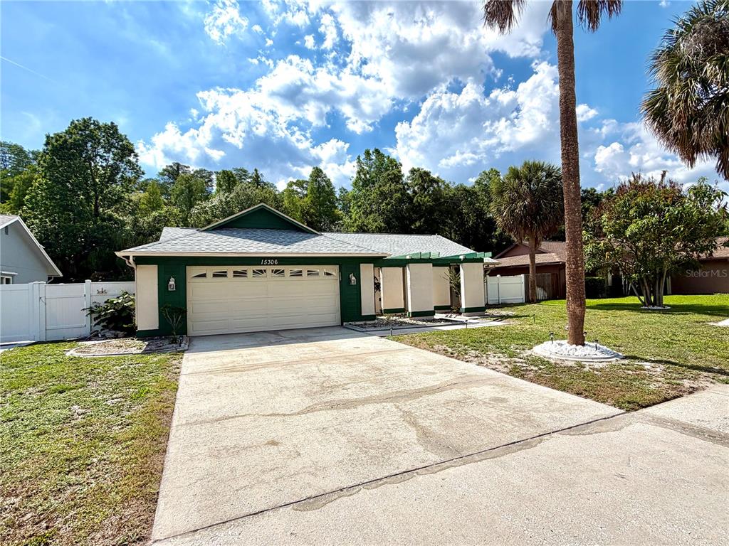A single-story house with a green exterior, a two-car garage, and a concrete driveway — 15306 WINTERWIND DRIVE, TAMPA, FL