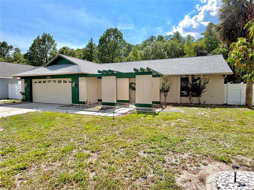 A single-story house features a beige exterior with green trim and a front pergola — 15306 WINTERWIND DRIVE, TAMPA, FL