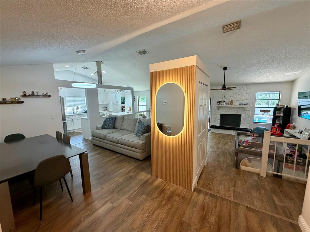 An open-concept living area features wood-look flooring, a dining table, and a central accent wall — 15306 WINTERWIND DRIVE, TAMPA, FL
