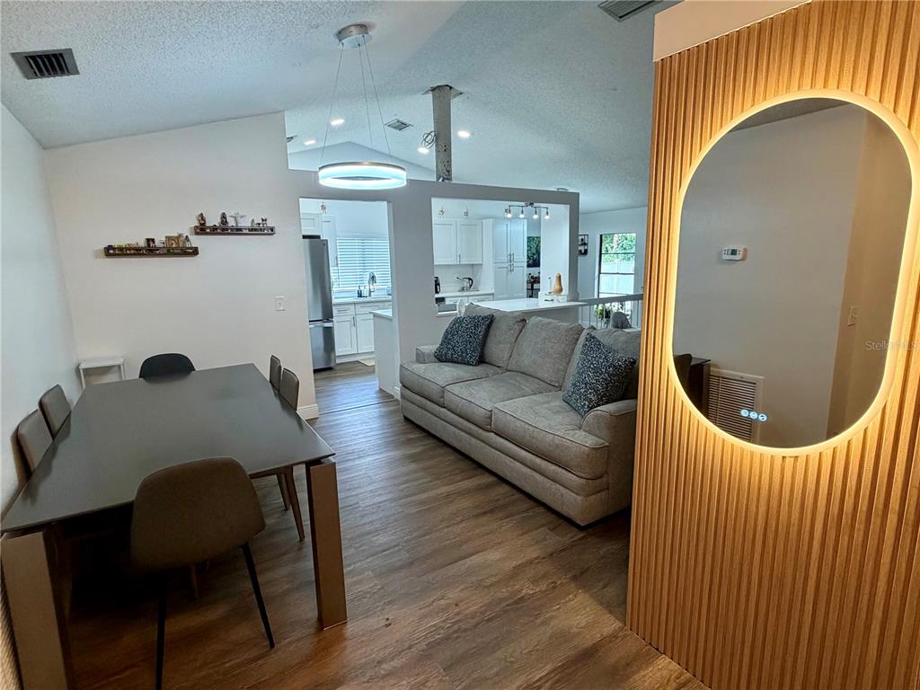 A dining area and living room feature wood-look flooring, a grey sofa, and a backlit mirror — 15306 WINTERWIND DRIVE, TAMPA, FL