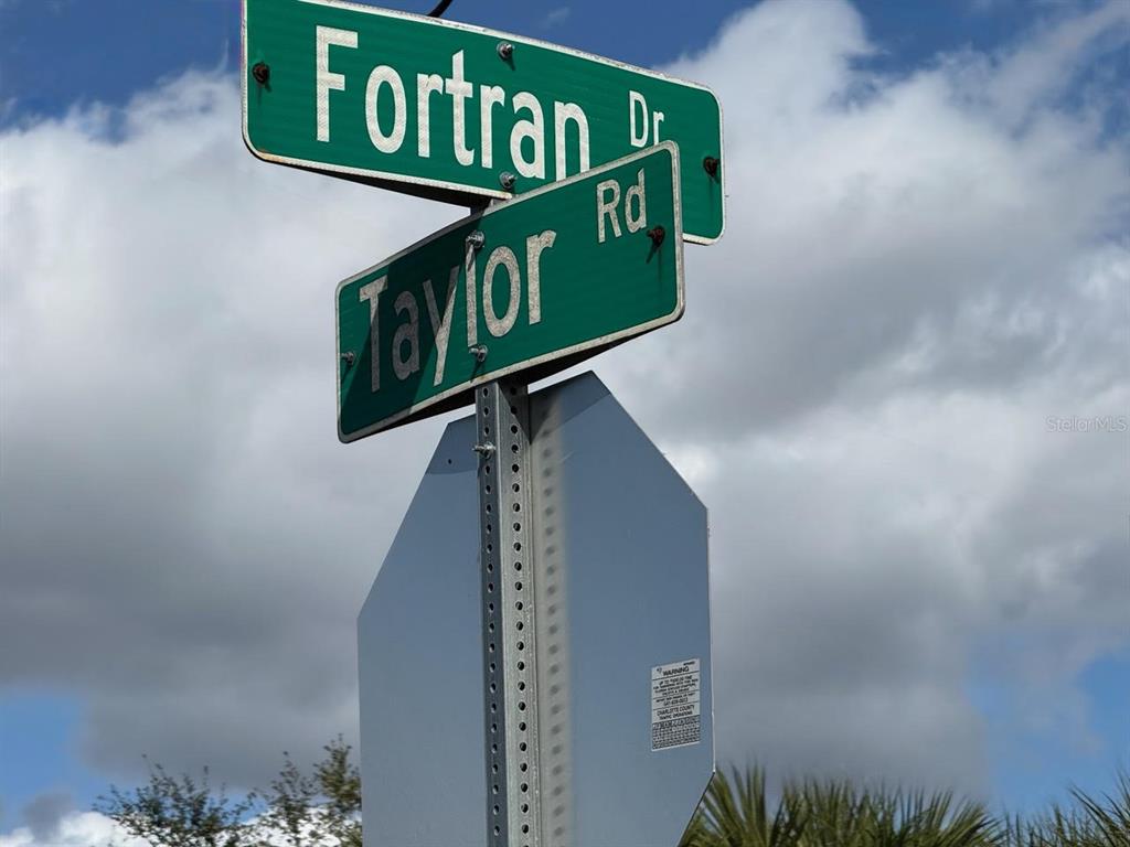 A street sign shows the intersection of Fortran Drive and Taylor Road against a cloudy sky — 25360 FORTRAN DRIVE, PUNTA GORDA, FL