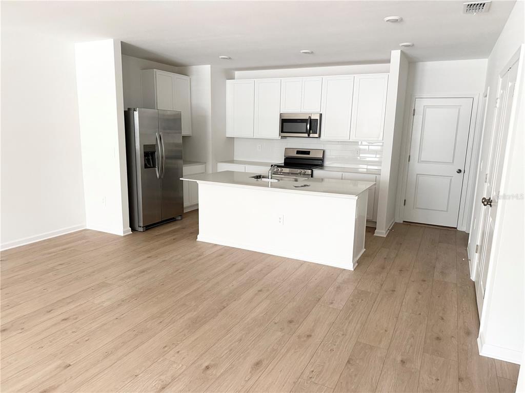 A modern kitchen features white cabinetry, stainless steel appliances, a center island, and wood flooring — 5178 CLAY WHALEY ROAD, ST CLOUD, FL