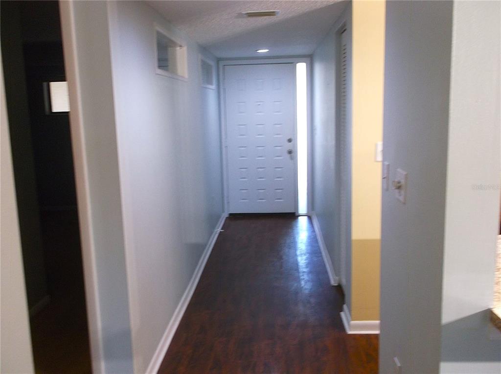 A hallway with dark wood-look flooring leads to a white front door with a sidelight — 9433 HARBOR GREENS WAY UNIT 305, SEMINOLE, FL