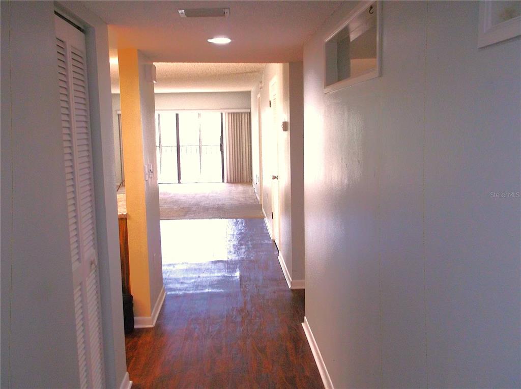 A hallway with wood-look flooring leads to a living area with a sliding glass door — 9433 HARBOR GREENS WAY UNIT 305, SEMINOLE, FL