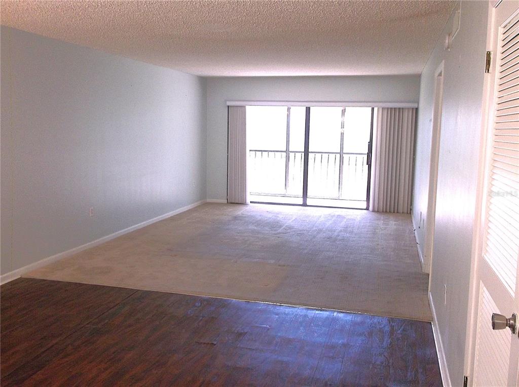 A living room features a combination of wood-look flooring and carpet with a sliding glass door — 9433 HARBOR GREENS WAY UNIT 305, SEMINOLE, FL