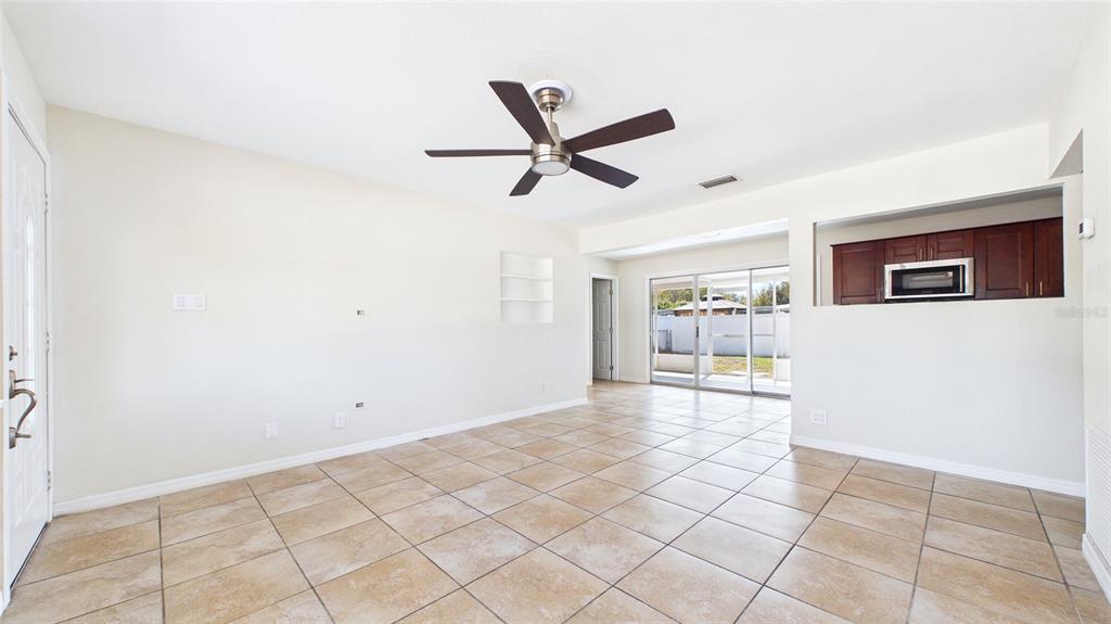 A living room with beige tile flooring, a ceiling fan, and an open kitchen pass-through — 4418 W FAIRVIEW HEIGHTS, TAMPA, FL
