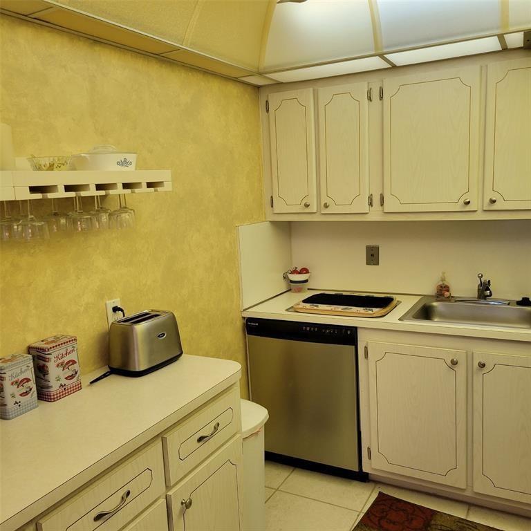 A small kitchen features white cabinets, a stainless steel dishwasher, and a yellow-painted wall — 351 Markham P # 351, Deerfield Beach FL 33442, DEERFIELD BEACH, FL