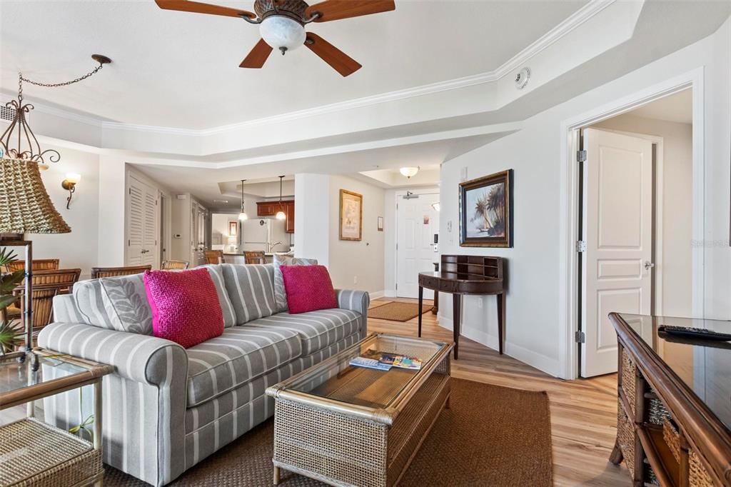 A living room features a striped sofa with pink pillows, a wicker coffee table, and wood-look flooring — 200 OCEAN CREST DRIVE UNIT 705, PALM COAST, FL