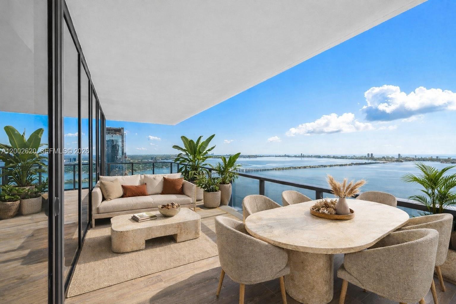 A furnished balcony features a seating area and dining table overlooking a bay and city — 788 NE 23rd St # 4802, Miami FL 33137, MIAMI, FL