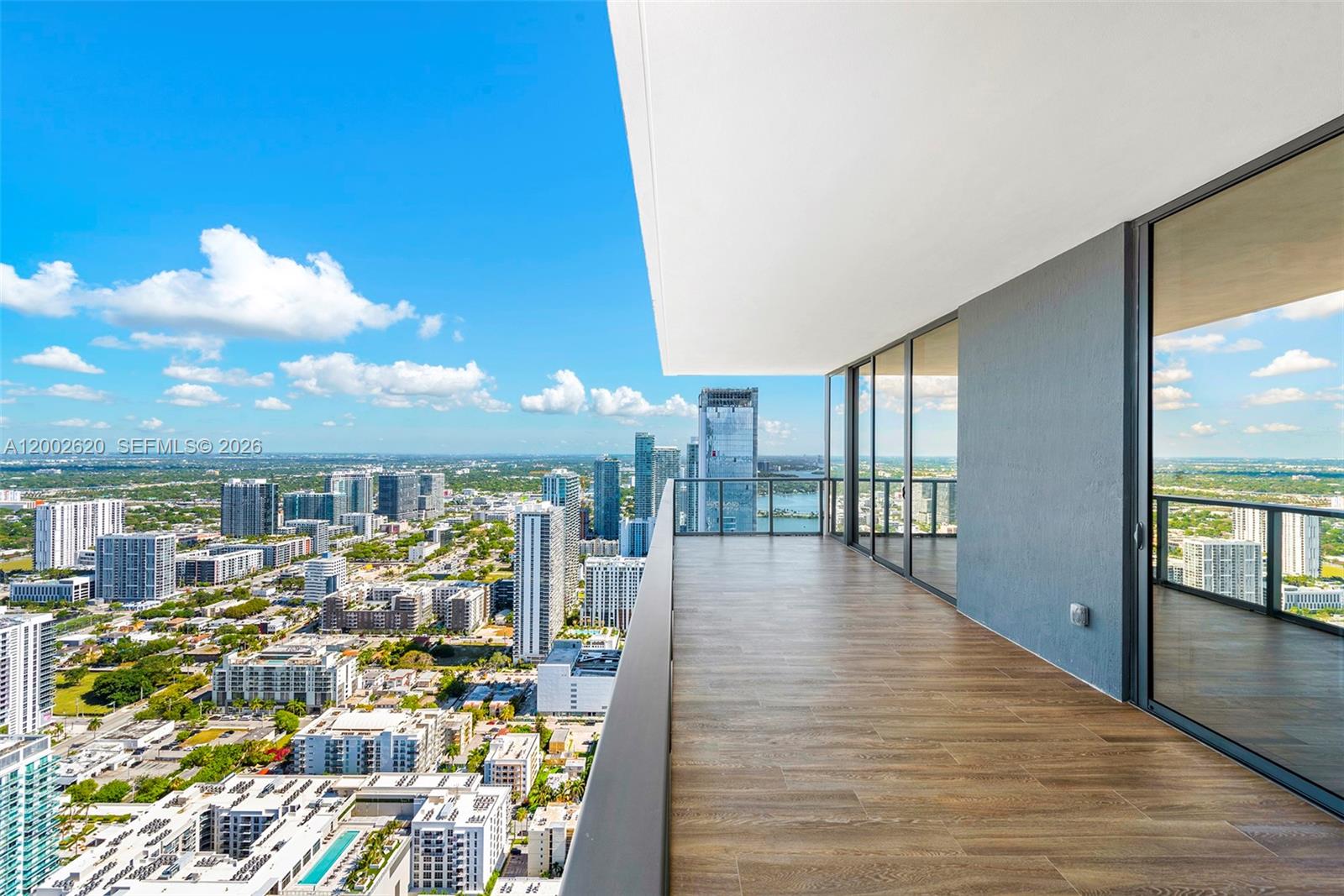 A high-rise balcony with wood-look tile flooring overlooks a dense urban cityscape and water — 788 NE 23rd St # 4802, Miami FL 33137, MIAMI, FL