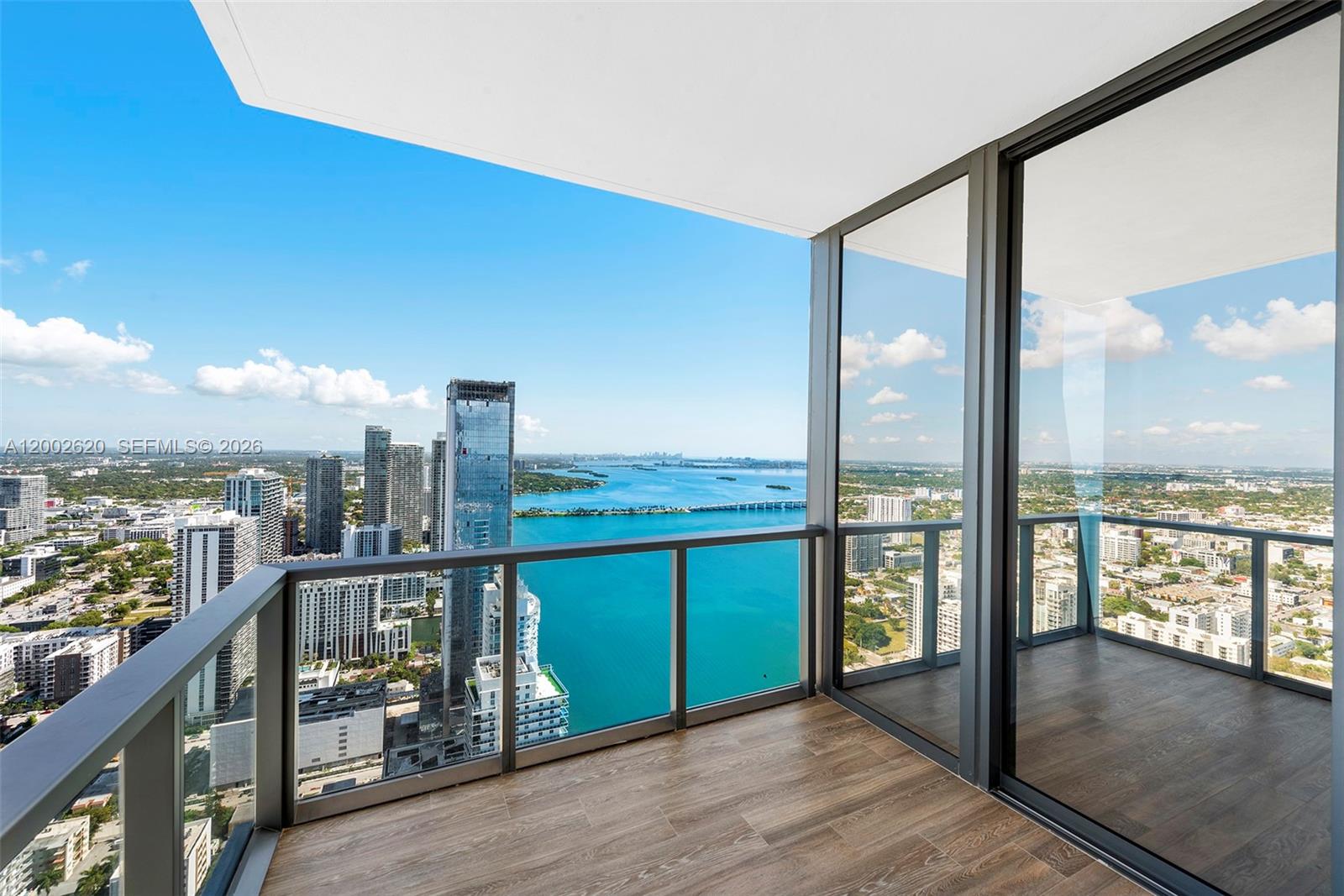 A high-rise balcony with wood-look flooring overlooks a city skyline and a blue bay — 788 NE 23rd St # 4802, Miami FL 33137, MIAMI, FL