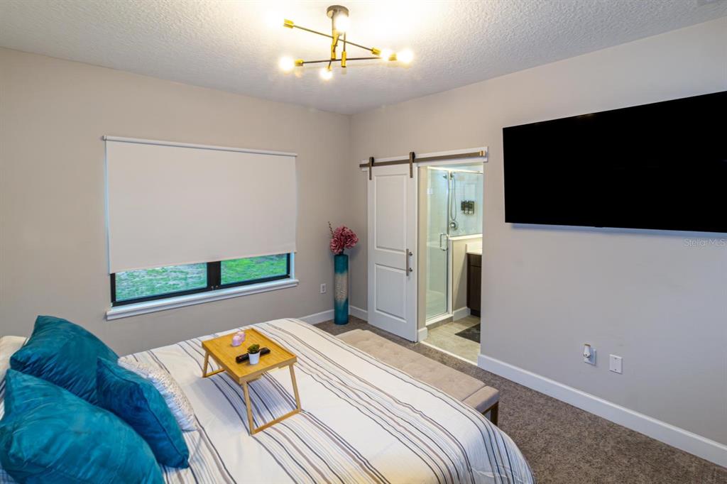 A bedroom features a bed with blue pillows, a sliding barn door, and a wall-mounted television — 136 VILLA DOMANI CIRCLE, DAVENPORT, FL