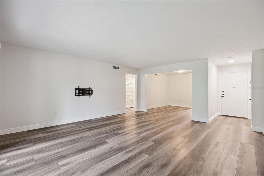 An empty living room features light gray walls, wood-look flooring, and a wall-mounted television bracket — 4300 LAKE UNDERHILL ROAD UNIT 23B2, ORLANDO, FL