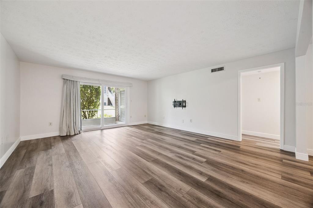 An empty living room features light gray walls, wood-look flooring, and a sliding glass door — 4300 LAKE UNDERHILL ROAD UNIT 23B2, ORLANDO, FL