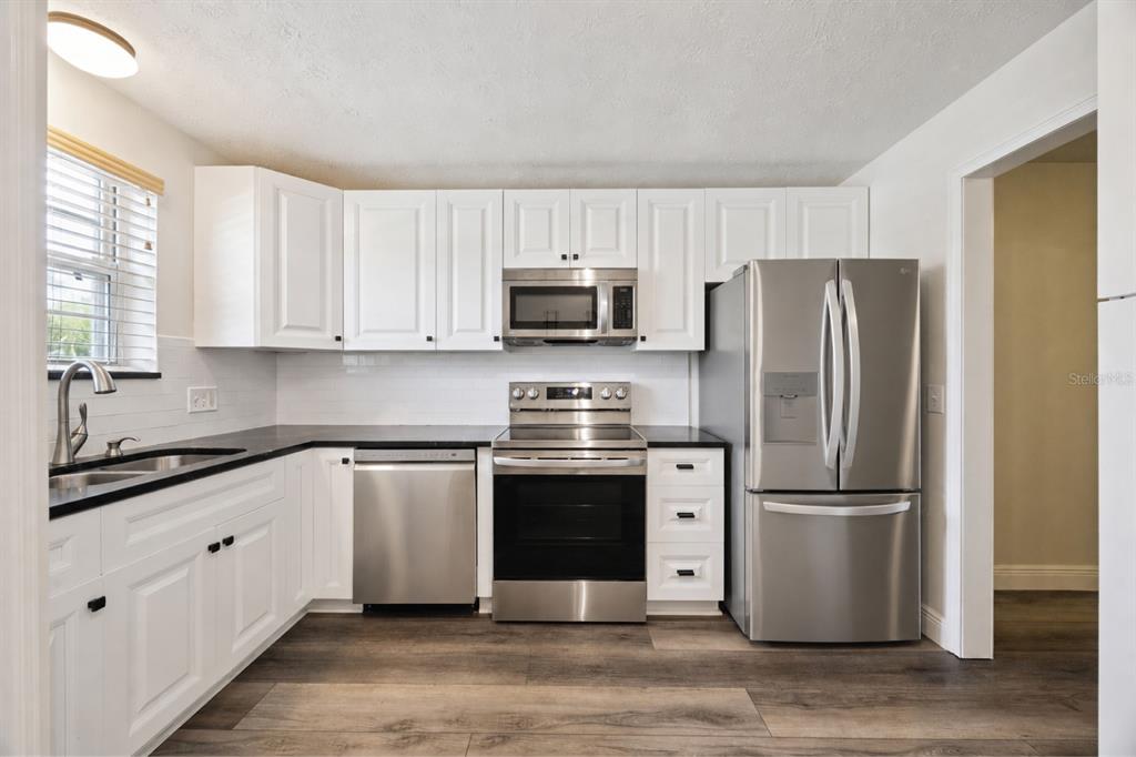 A kitchen with white cabinets, stainless steel appliances, black countertops, and wood-look flooring — 4300 LAKE UNDERHILL ROAD UNIT 23B2, ORLANDO, FL