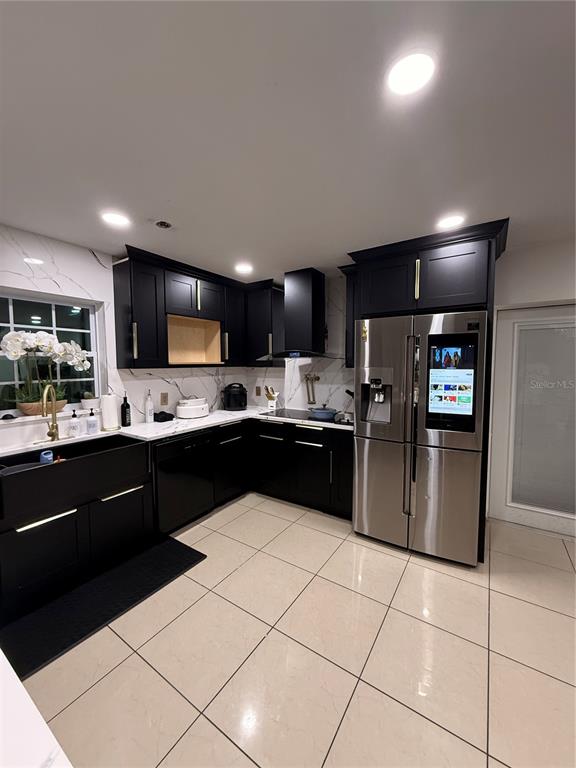 A modern kitchen features black cabinetry, white marble-style countertops, and a stainless steel smart refrigerator — 1305 E LOUISE AVENUE, TAMPA, FL