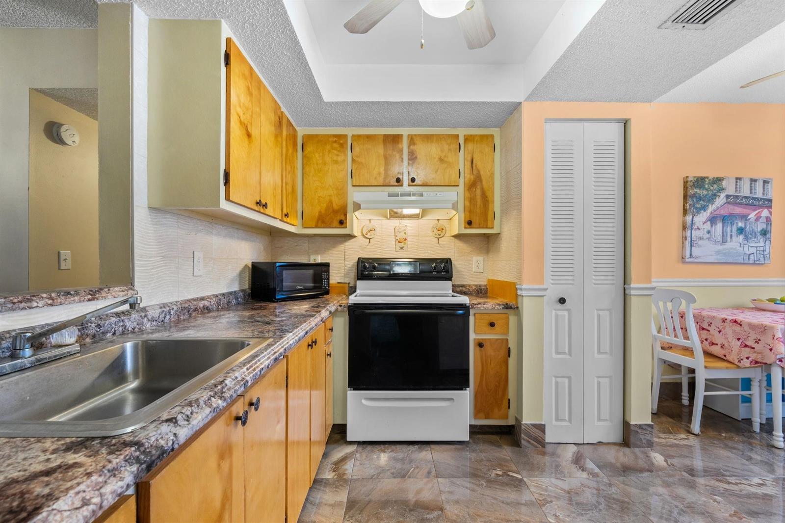 A kitchen with light wood cabinets, a black stove, and a marble-patterned countertop — 10 Willowbrook Lane # 108, Delray Beach FL 33446, DELRAY BEACH, FL