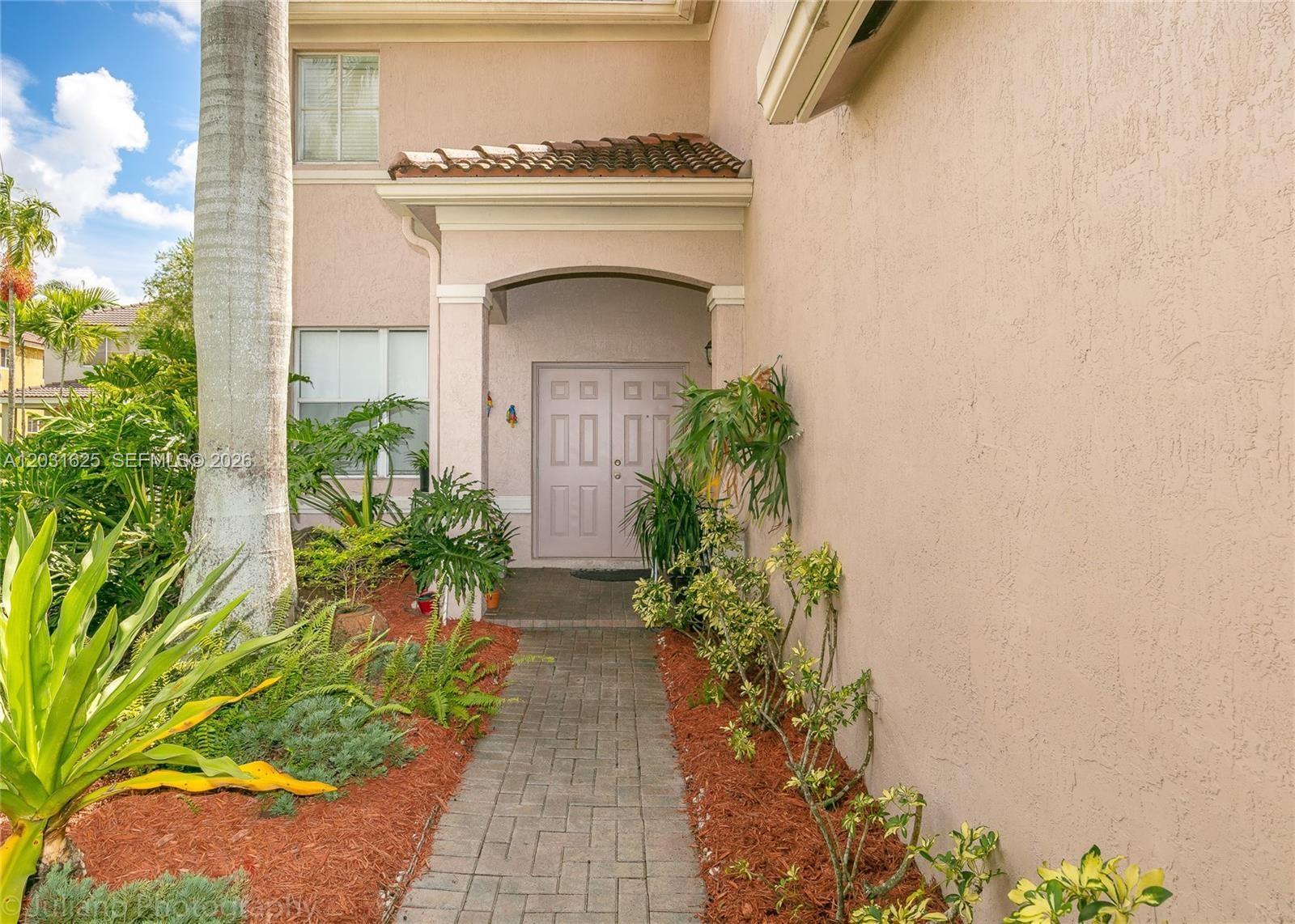 A paved walkway leads to the double front doors of a tan stucco home — 1032 Silktree Ln, Weston FL 33327, WESTON, FL