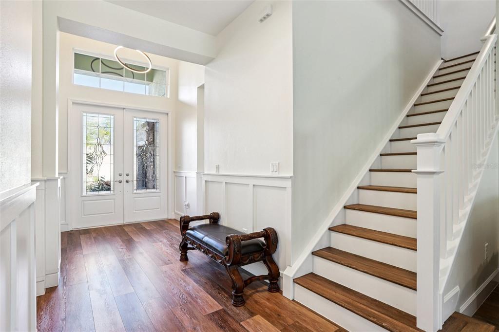 An entryway features wood flooring, a dark leather bench, and a staircase with white railings — 3326 ACACIA BAY AVENUE, WESLEY CHAPEL, FL