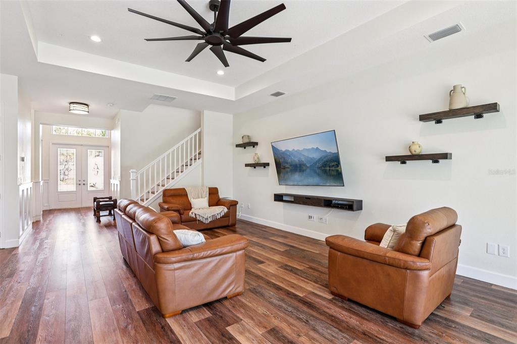 A living room features brown leather furniture, wood-look flooring, a wall-mounted television, and floating shelves — 3326 ACACIA BAY AVENUE, WESLEY CHAPEL, FL