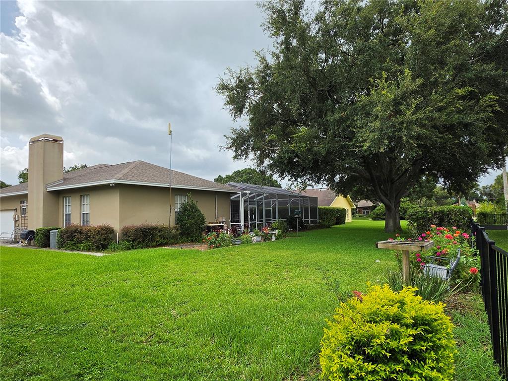 A backyard view of a house with a chimney, a screened-in patio, and large trees — 6523 CREWS LAKE HILLS LOOP E, LAKELAND, FL