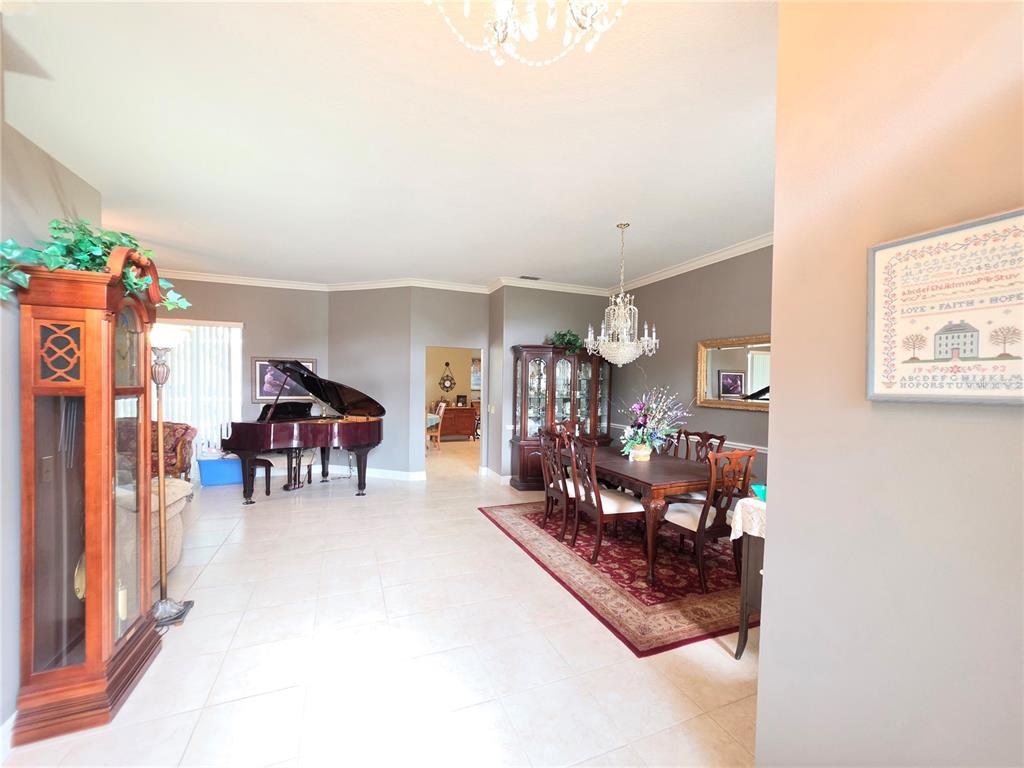 A dining room and living area feature a grand piano, chandelier, and tile flooring — 6523 CREWS LAKE HILLS LOOP E, LAKELAND, FL