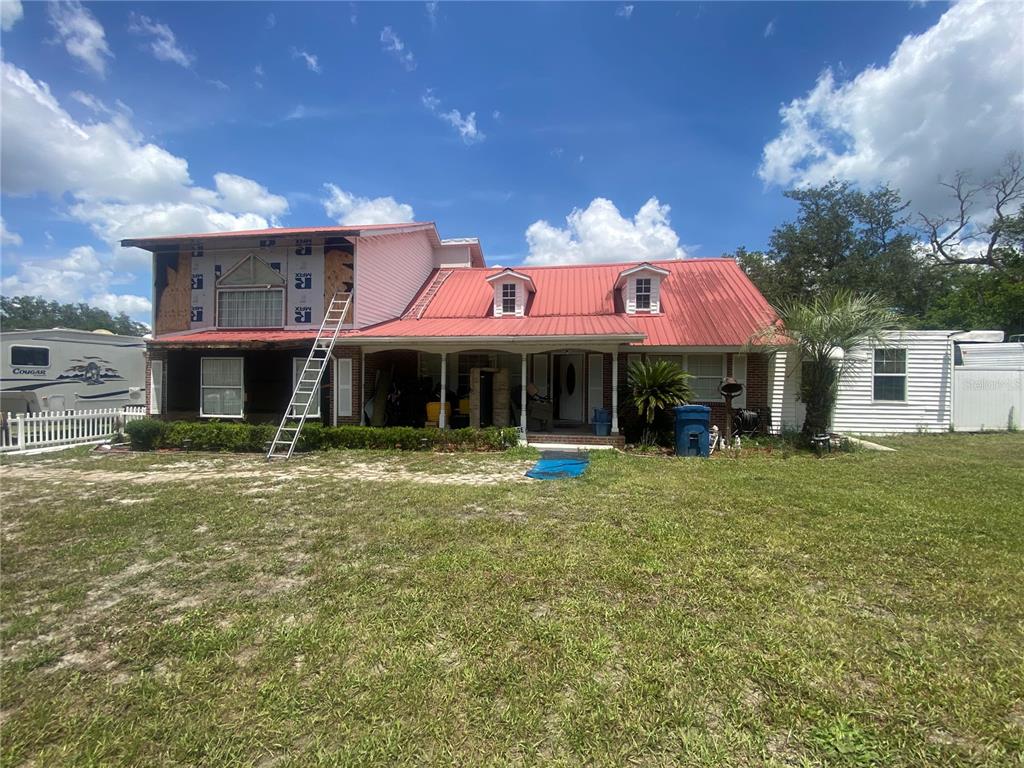 A two-story house with a red metal roof and unfinished siding on the left side — 219 SHADY LANE, ORANGE CITY, FL